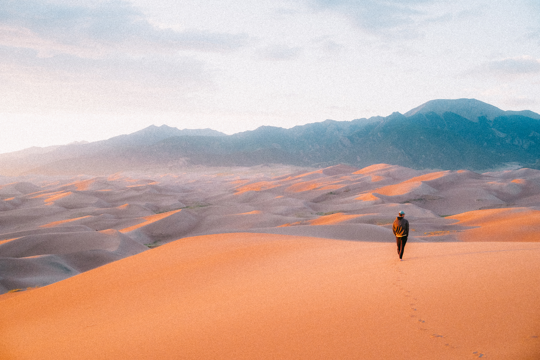 Solo hiker walking across sand dunes at sunset